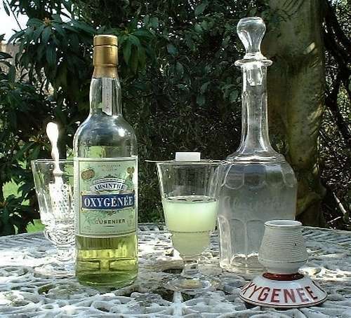 бутылка абсента на столе, графин воды и бокалы с напитком и кусочками рафинада