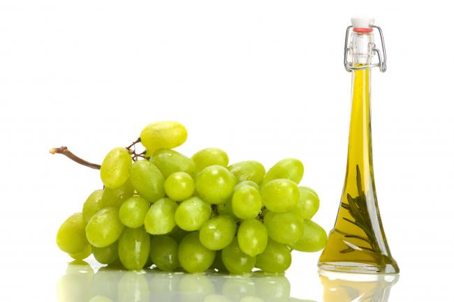 гроздь белого винограда и масло из косточек в высокой бутылке